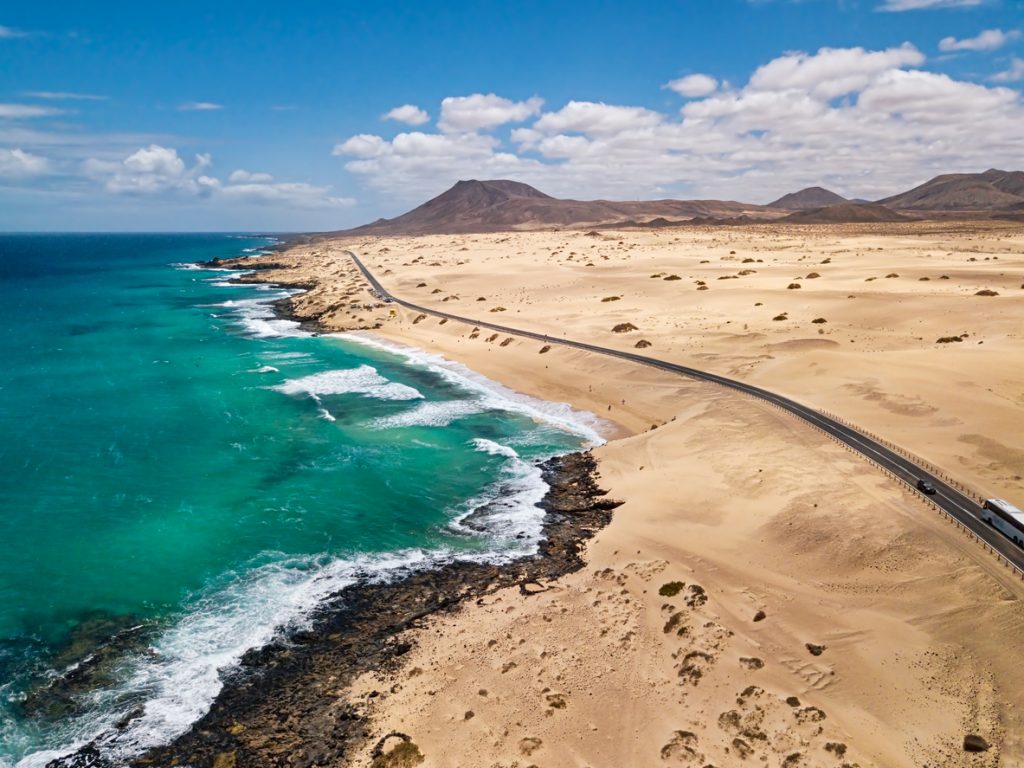 Weitläufiger Strand Alzada im Corralejo Naturpark auf Fuerteventura mit Sanddünen, Küstenstraße und türkisfarbenem Meer.