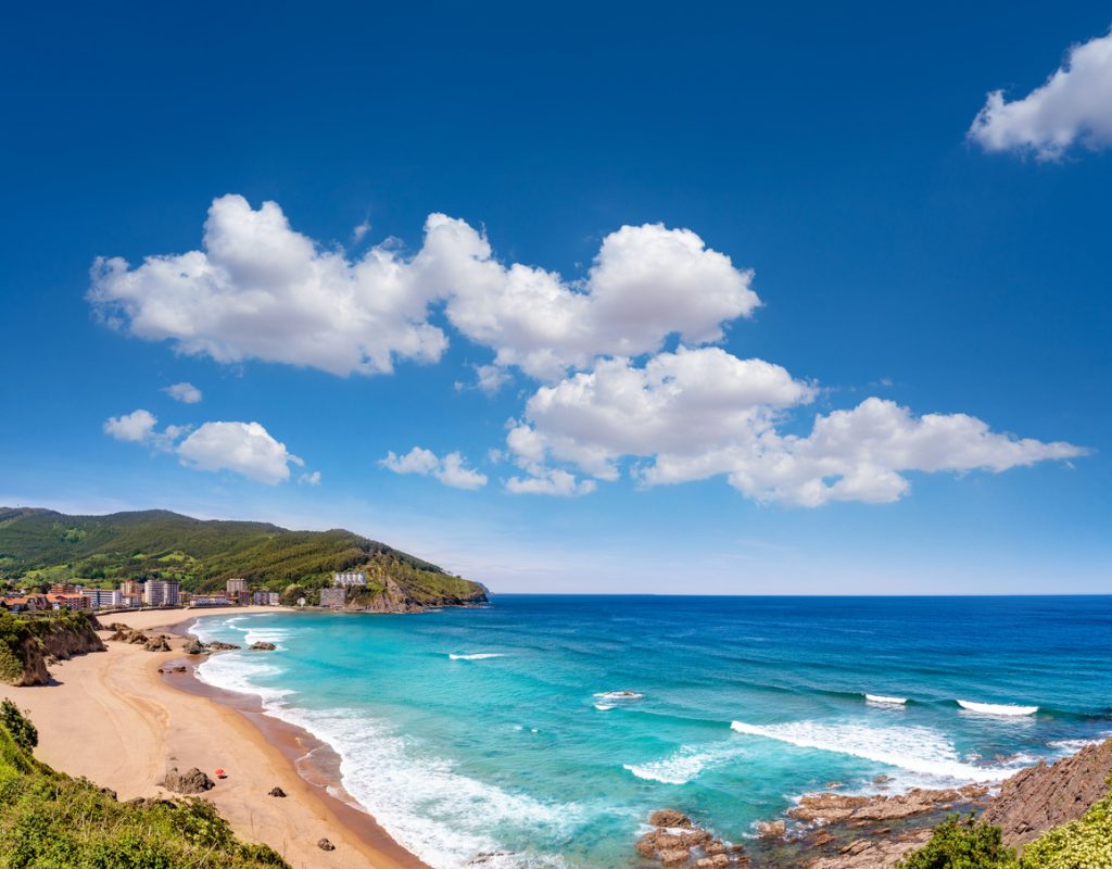 Panoramablick auf den Strand von Bakio nahe Bilbao mit goldenem Sandstrand, türkisfarbenem Meer und grünen Hügeln im Baskenland.