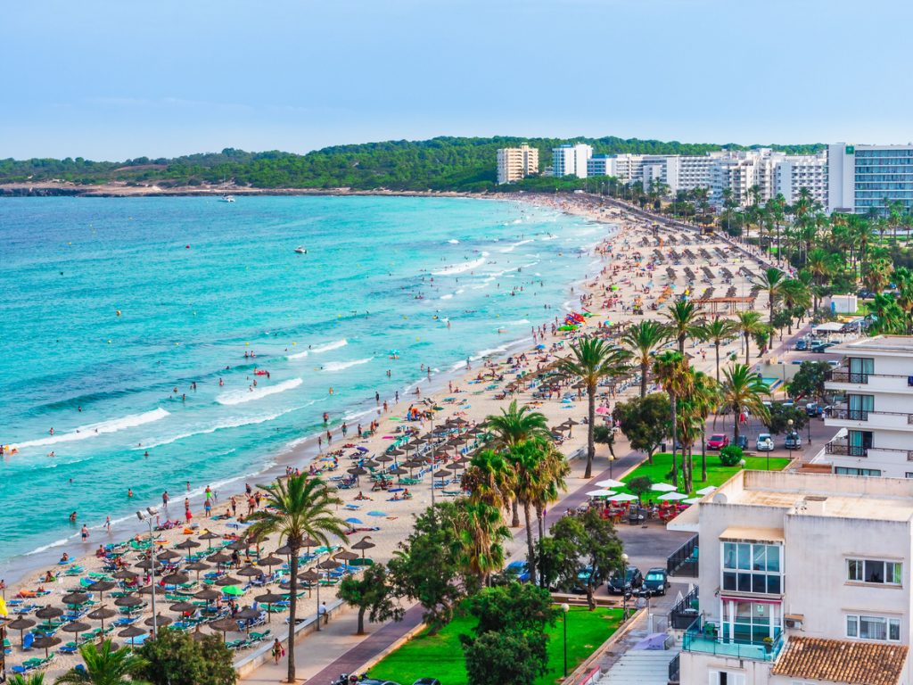 Strand von Cala Millor auf Mallorca mit türkisblauem Meer, Palmenpromenade und Hotels im Hintergrund.