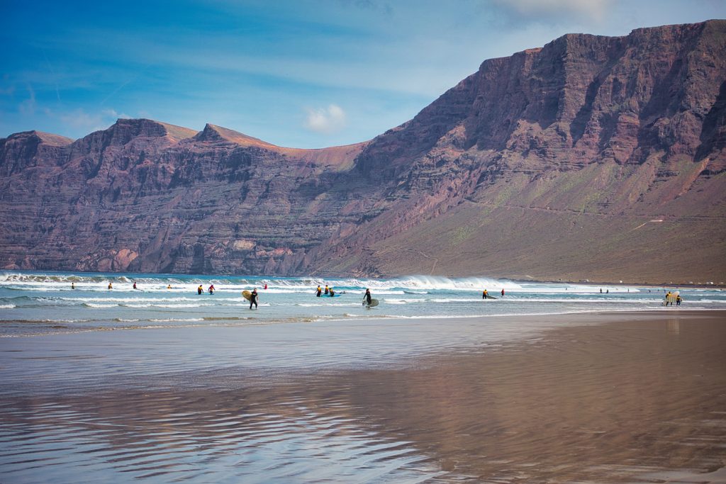 Surfer am Playa de Famara auf Lanzarote mit Blick auf die hohen Felsen und den weiten Sandstrand.