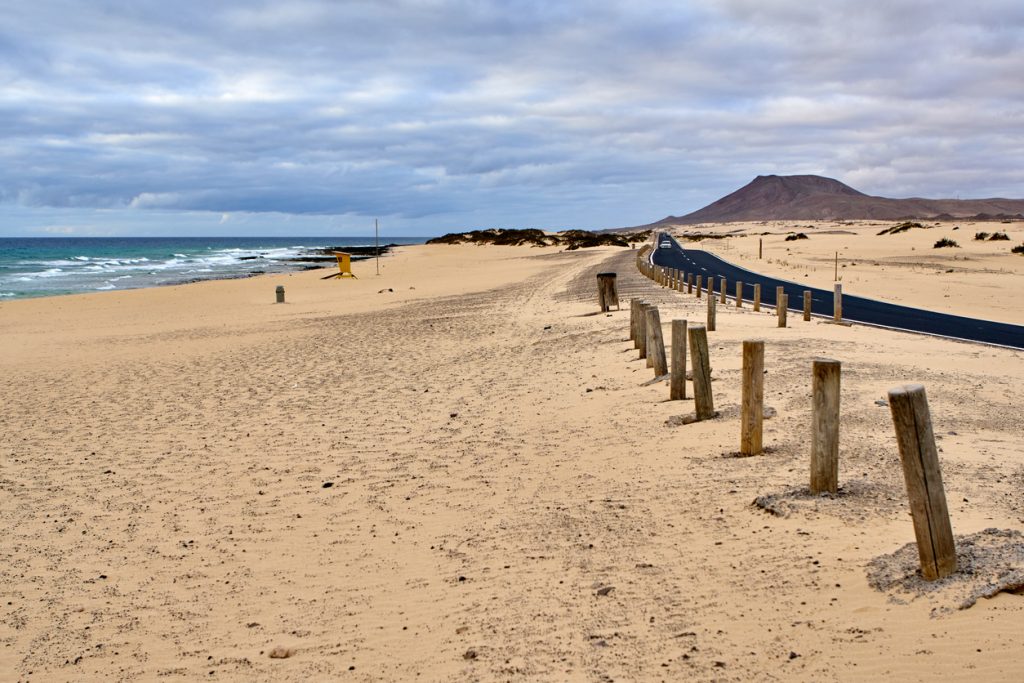 Weitläufiger Corralejo Strand auf Fuerteventura mit Sanddünen, Atlantikwellen und Küstenstraße.
