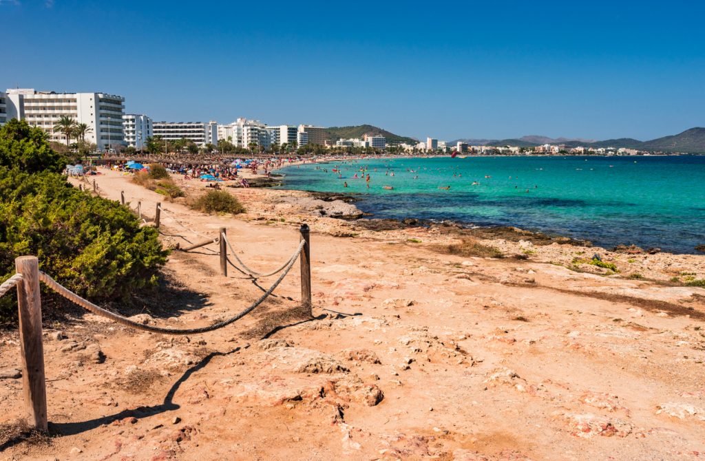 Panoramablick auf den Strand von Cala Millor auf Mallorca mit Hotels, Besuchern und türkisfarbenem Wasser.