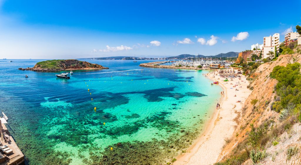 Panoramablick auf den Strand und den Yachthafen Puerto Portals in Portals Nous, Mallorca, mit türkisblauem Wasser und Badenden.