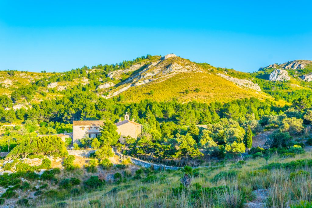 Steinkapelle Ermita de Betlem vor grünen Hügeln und blauem Himmel auf Mallorca.