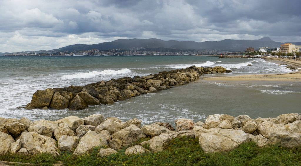 Wolkenverhangene Küste Mallorcas mit Wellen und Steinmole.