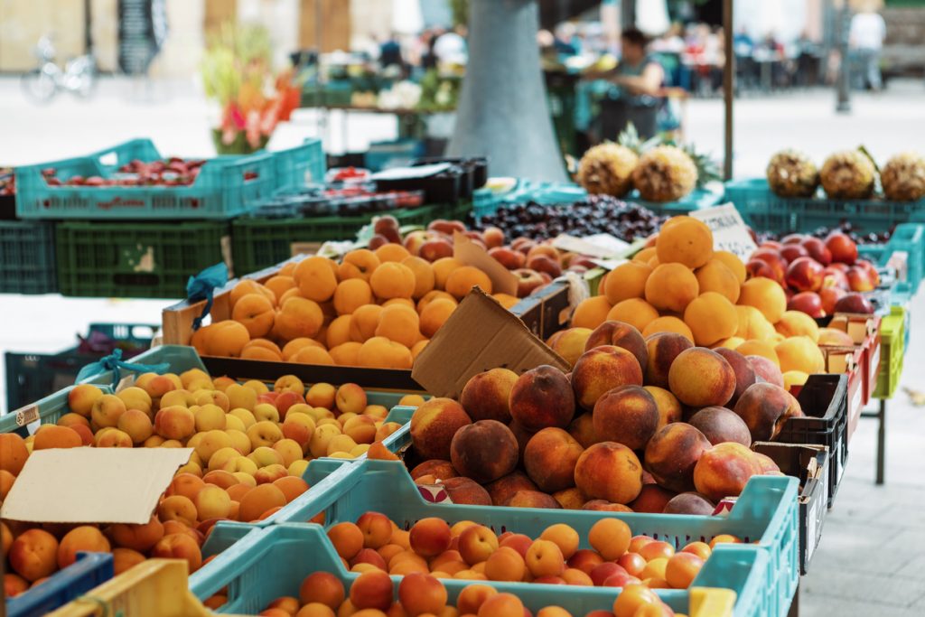 Obststände mit Kisten voller Pfirsiche, Aprikosen und anderem saisonalen Obst auf einem mallorquinischen Wochenmarkt.