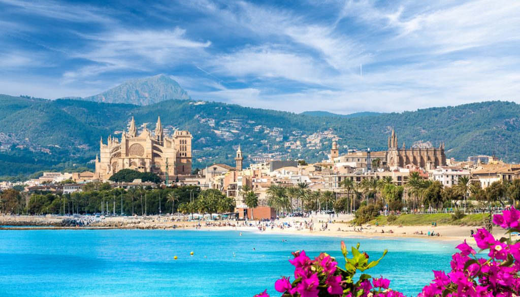 Blick über Palma de Mallorca mit der gotischen Kathedrale La Seu, Strandpromenade, türkisblauem Meer und der Serra de Tramuntana im Hintergrund.