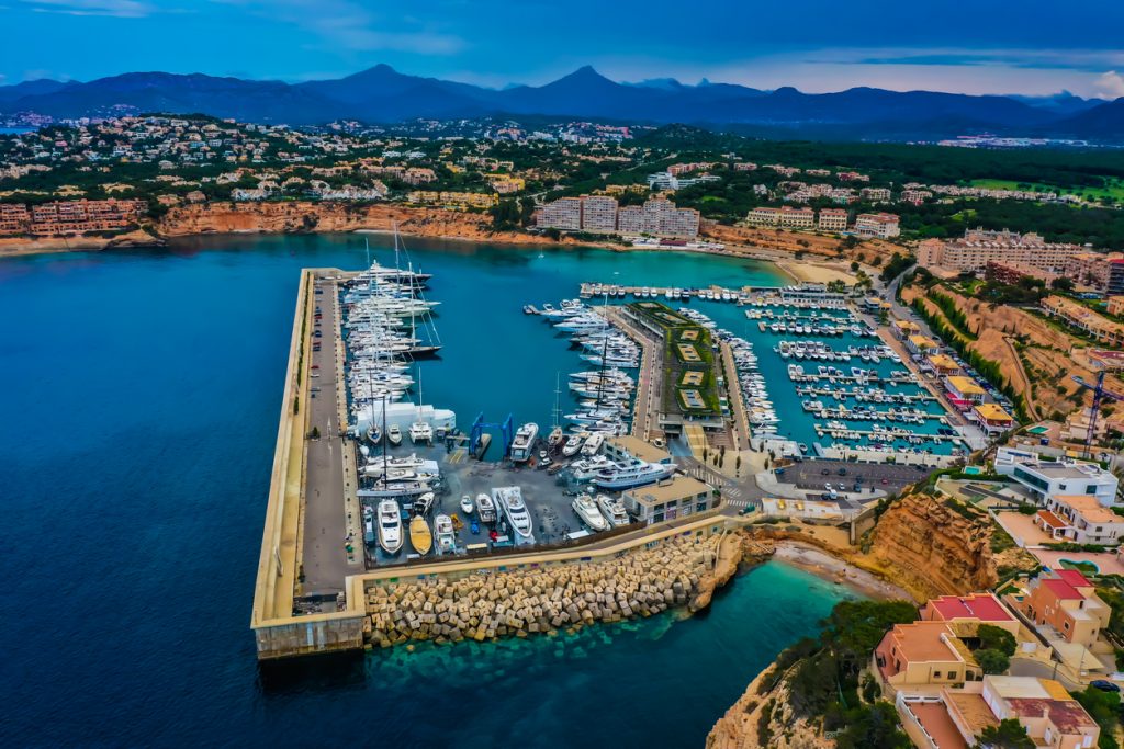 Drohnenaufnahme des Yachthafens Port Adriano mit langem Wellenbrecher, Superyachten und der Bucht von El Toro.