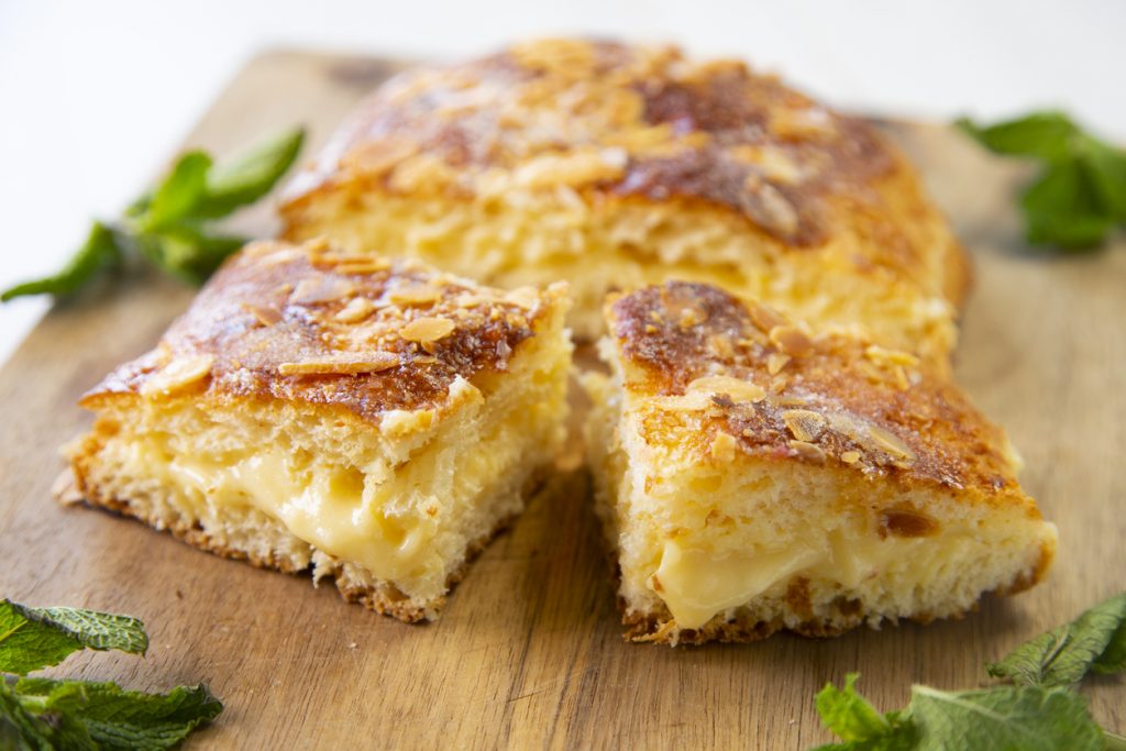 Aufgeschnittene Coca de Sant Joan mit goldener Oberfläche und heller Vanillecreme auf einem Holzbrett.