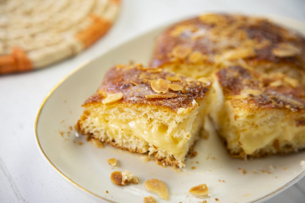 Stücke einer Coca de Sant Joan mit cremiger Füllung und gerösteten Mandelblättchen auf einem Teller.