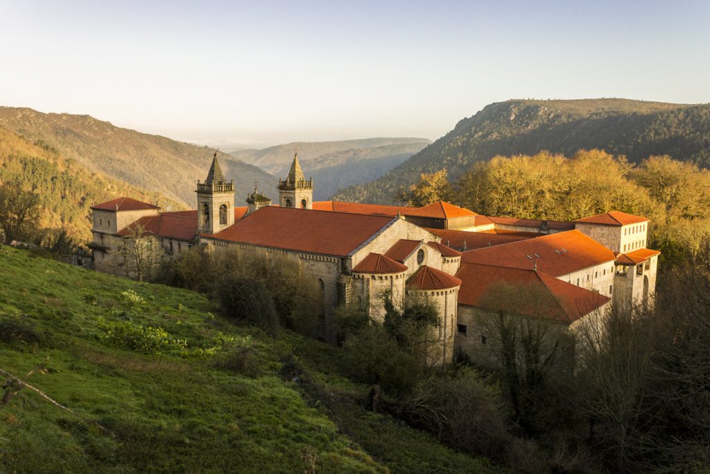 Großes Kloster mit roten Ziegeldächern und zwei Türmen liegt an einem Hang, umgeben von Wäldern und Schluchten.