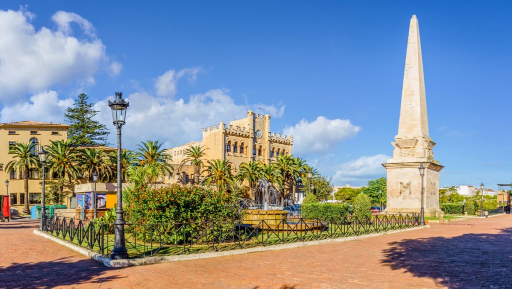 Platz mit Obelisk, Palmen, Springbrunnen und historischem Rathaus auf Menorca.