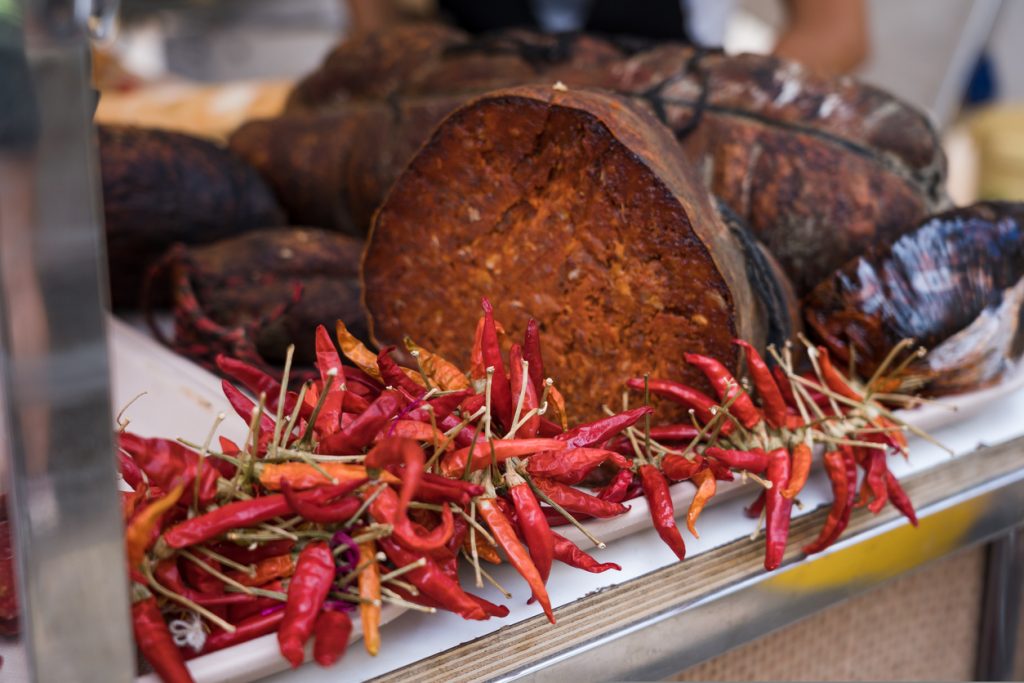 Aufgeschnittene Sobrassada mit einer Girlande roter Chilischoten an einem mallorquinischen Marktstand.
