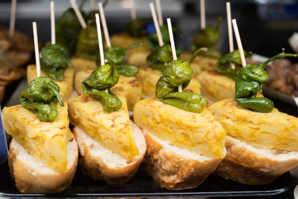 Dreieckige Tortilla auf Baguette, mit Padrón-Paprika und Zahnstocher.