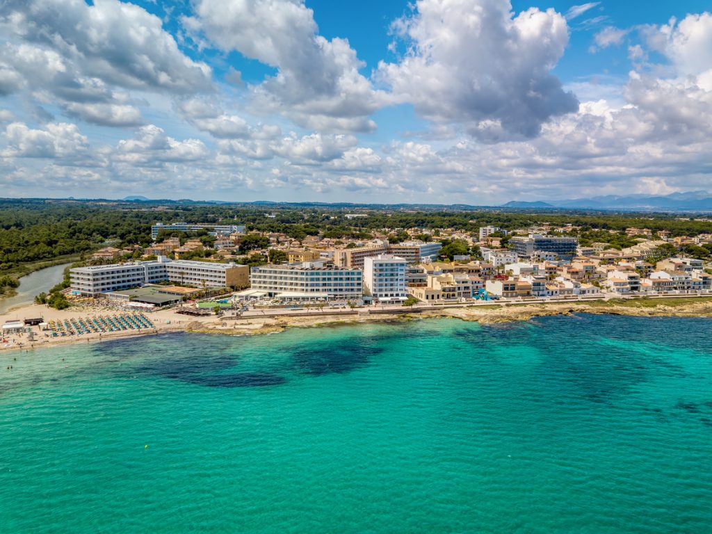 Luftaufnahme von Can Picafort mit Hotelkomplexen, Strandliegen und türkisblauem Meer.