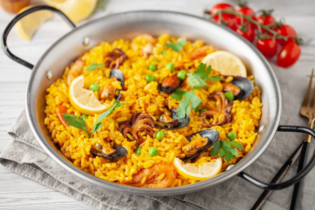 Eine Pfanne mit gelber Meeresfrüchte-Paella mit Muscheln, Garnelen, Erbsen und Zitronenscheiben.