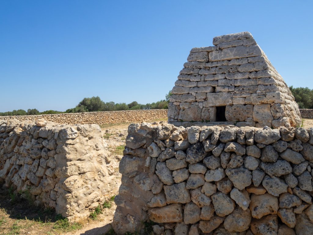 Bootsförmiges Steingrab mit Trockenmauern unter blauem Himmel.