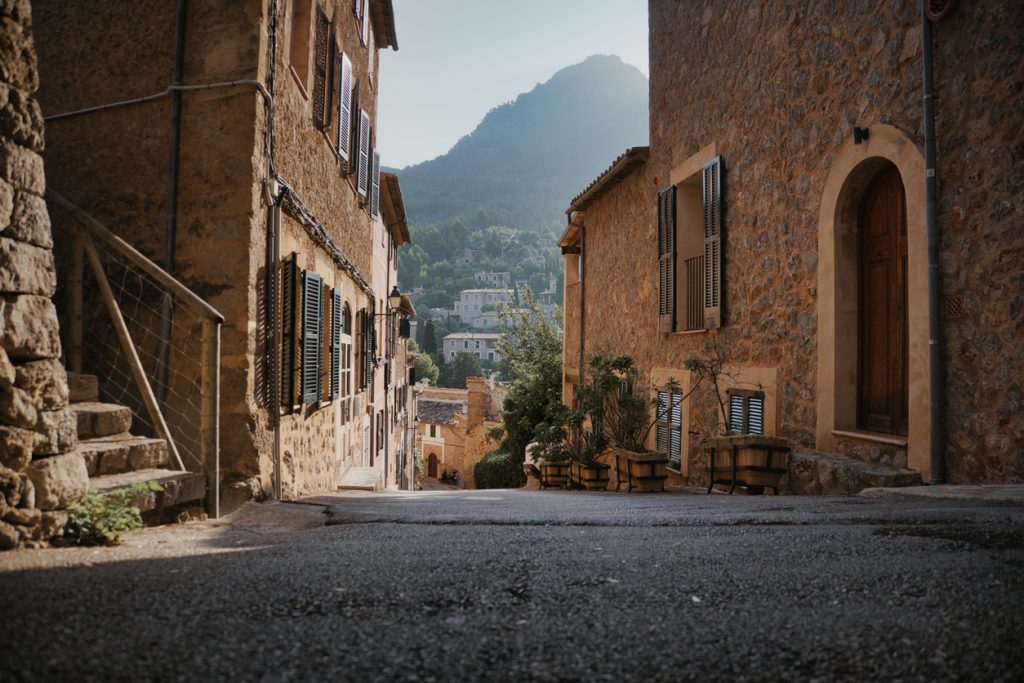 Enge Gasse zwischen Sandsteinhäusern in Deià mit Bergen im Hintergrund.
