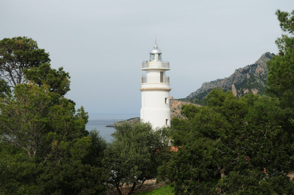 Weißer Leuchtturm Far del Cap Gros ragt über Pinien mit Blick auf das Meer und das Tramuntana-Gebirge.
