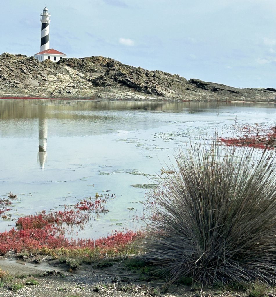 Schwarz-weiß geringelter Leuchtturm spiegelt sich im stillen Wasser.