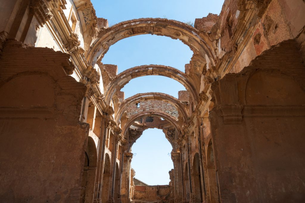 Verfallene Bögen und Mauerreste einer Kirche in Belchite öffnen sich zum wolkenlosen Himmel.