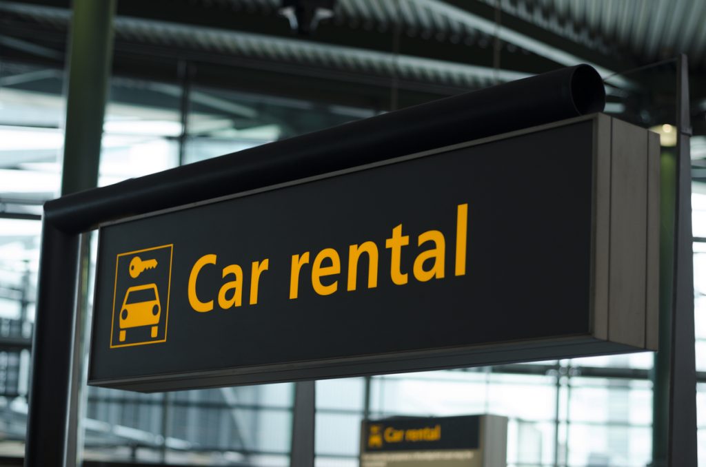 Schwarzes Flughafenschild „Car rental“ mit Schlüssel- und Auto-Symbol.