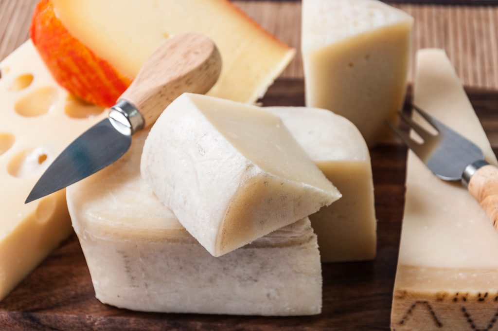 Mehrere Mahón-Stücke liegen auf einem Holzbrett mit Käsemessern