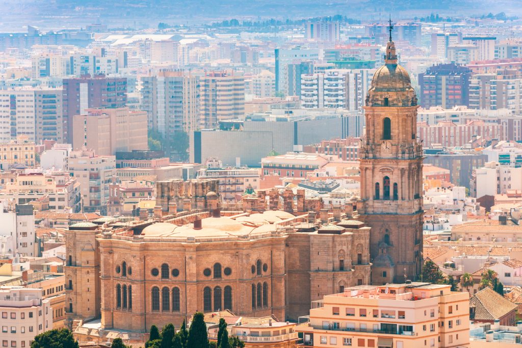 Der Kathedralturm von Málaga steht vor dichtem Stadtpanorama.