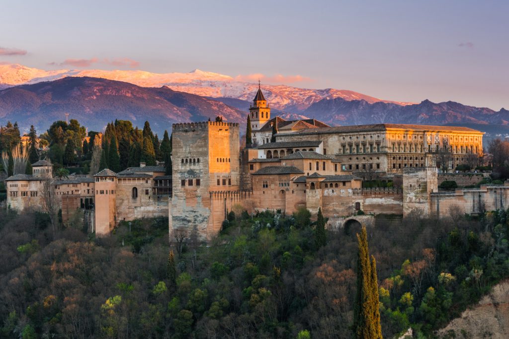 Panorama der Alhambra in Granada mit Türmen und Palast Karls V. vor schneebedeckten Bergen.