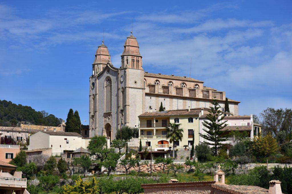 Die Kirche Sant Joan mit zwei Türmen erhebt sich über den Häusern von Calvià unter blauem Himmel.