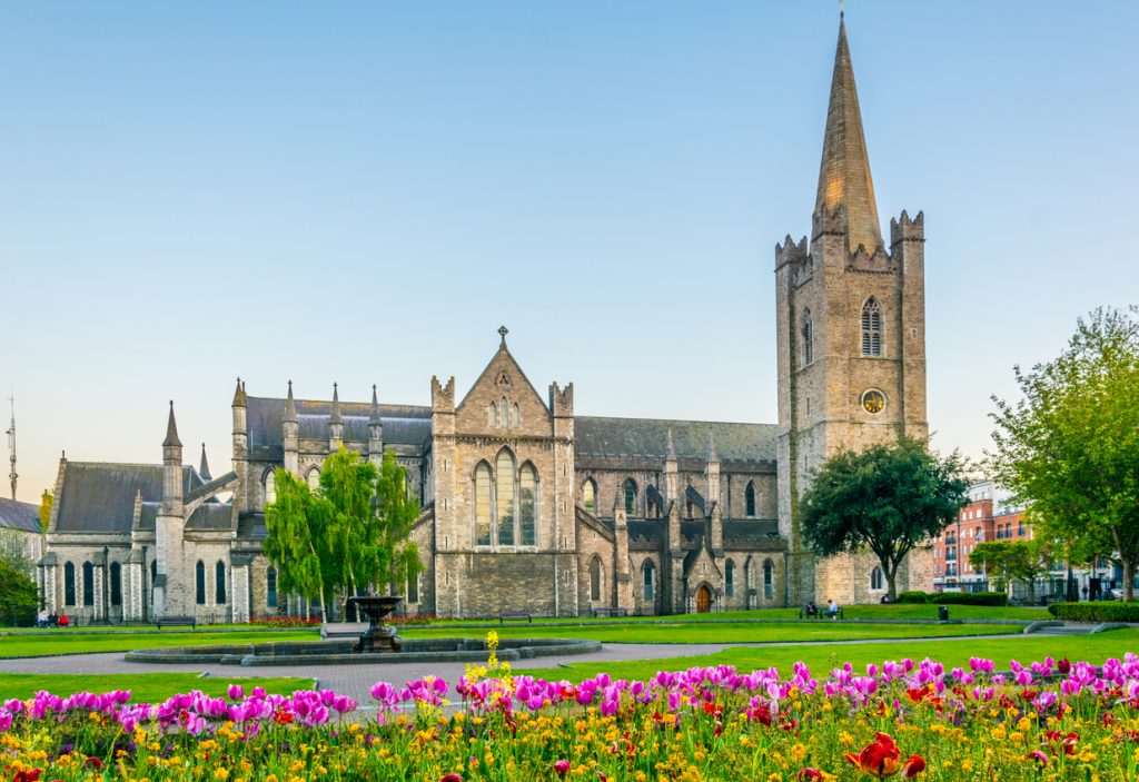 Gotische Kathedrale St Patrick’s in Dublin mit buntem Blumenbeet im Vordergrund.
