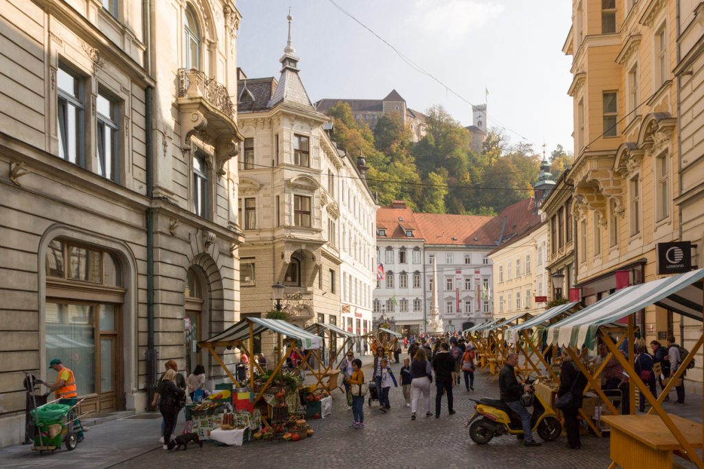 Belebte Fußgängerstraße mit Marktständen und Burg auf dem Hügel.