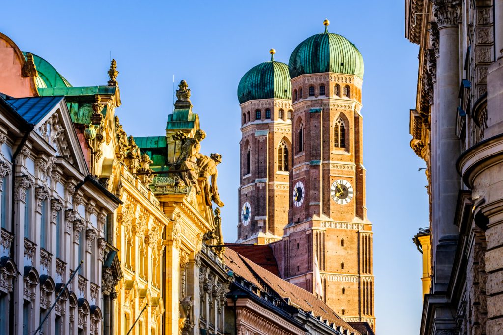 Die grünen Zwiebeltürme der Münchner Frauenkirche über historischen Fassaden.