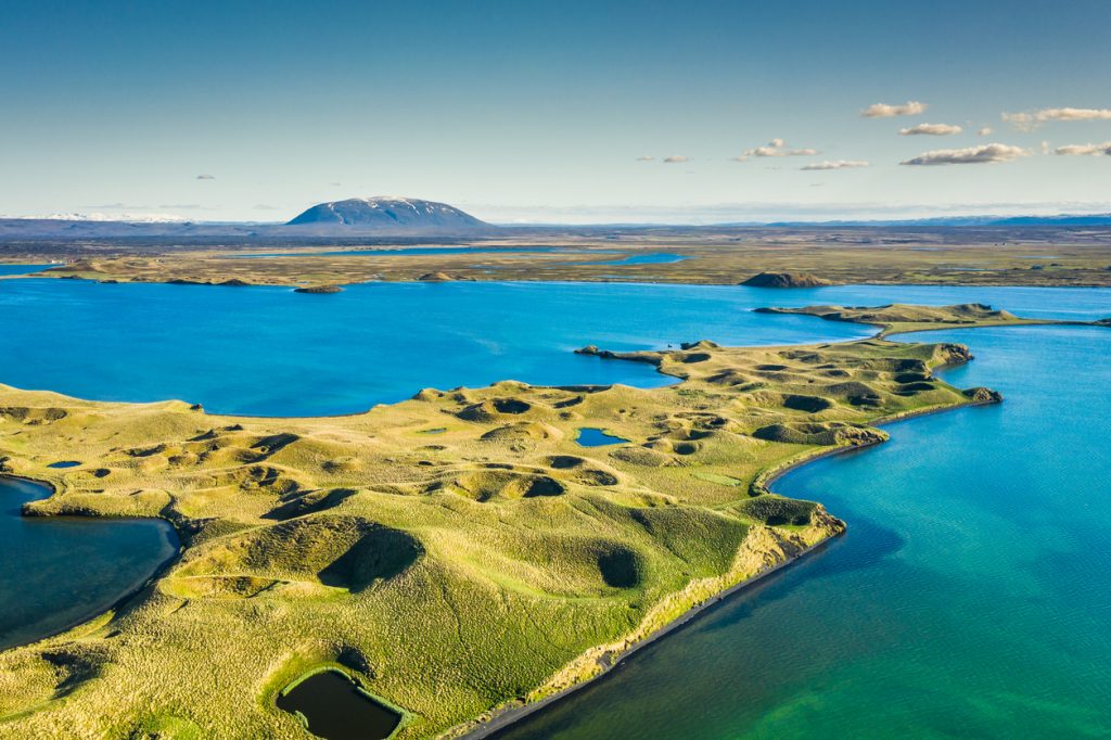 Luftaufnahme der Skútustaðagígar-Pseudokrater am See Mývatn mit türkisblauem Wasser und Hverfjall am Horizont.