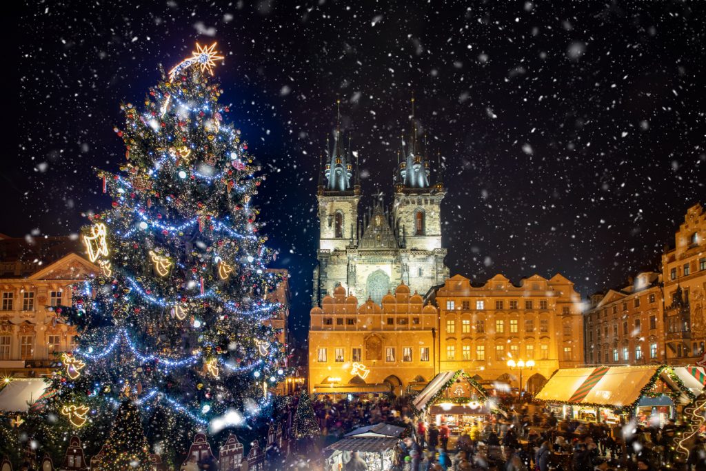 Großer Weihnachtsbaum und Marktstände vor der Teynkirche bei Nacht und Schnee.