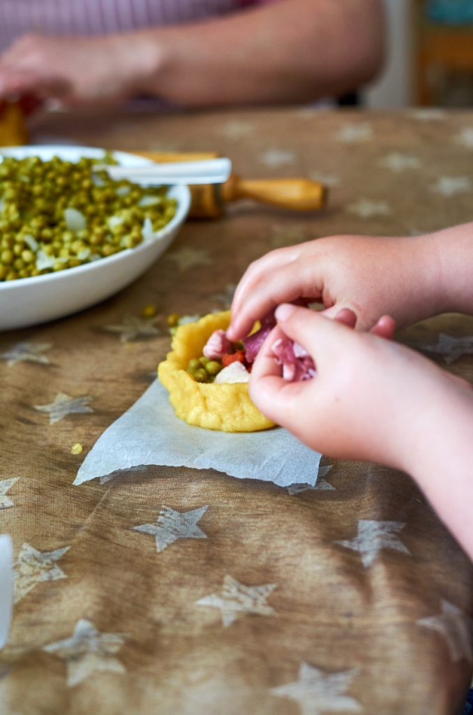 Kinderhände geben Fleisch und Erbsen in eine geformte Panada.