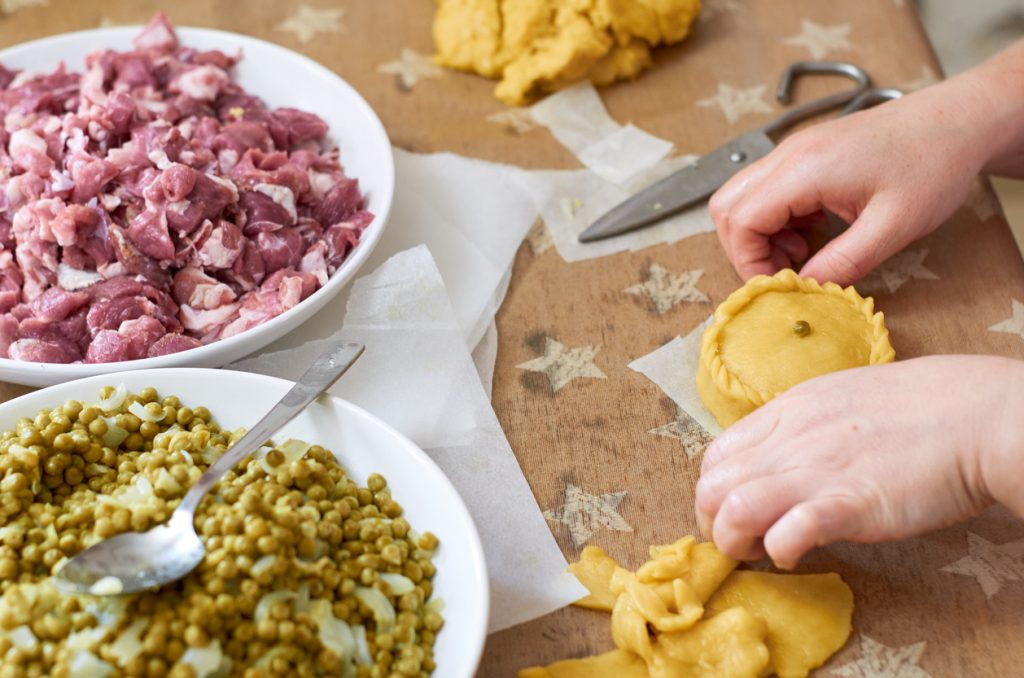 Hände formen eine ungebackene Panada, daneben Schüsseln mit Fleisch und Erbsen.