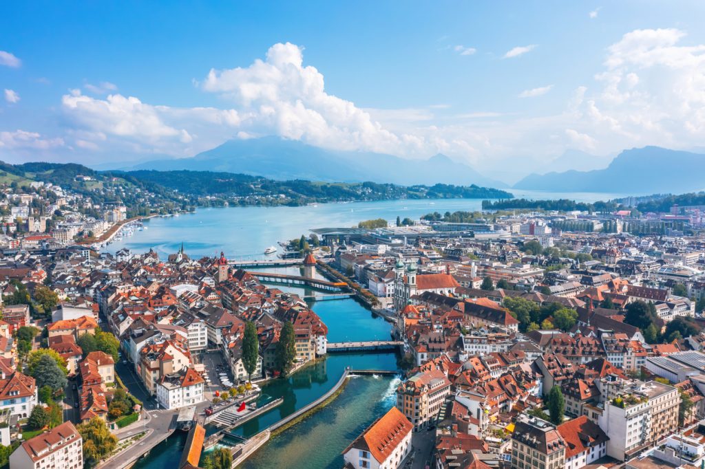 Panorama von Luzern mit Altstadt, Fluss, Brücken und dem Vierwaldstättersee vor Bergen.