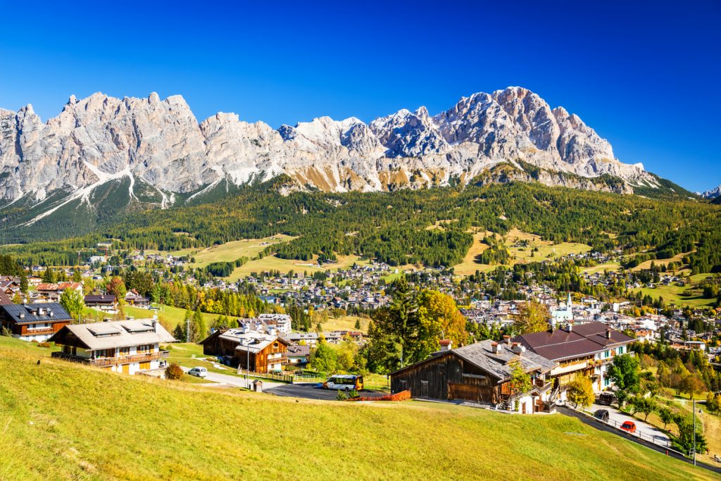 Blick über Chalets, Wiesen und die Stadt Cortina mit steiler Felskulisse.