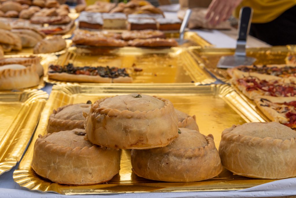 Mehrere goldbraune Panades liegen auf goldenen Tabletts an einem Marktstand.