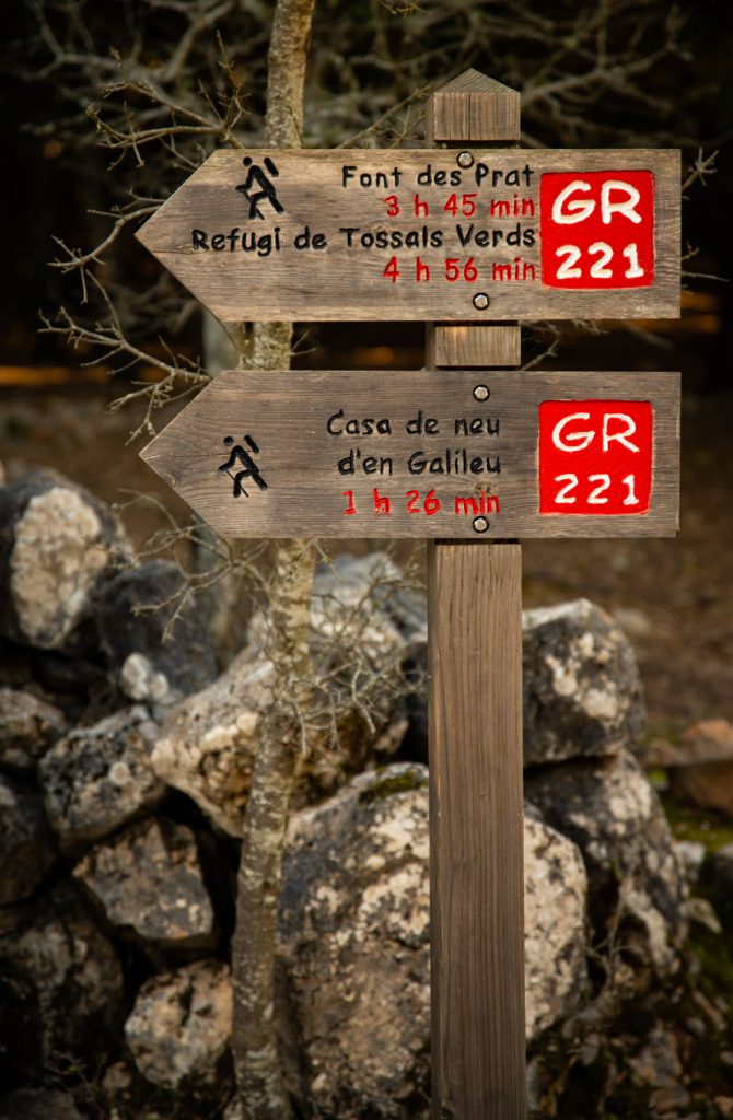 Holzpfeile zeigen Zeiten zur Font des Prat und zum Refugi de Tossals Verds