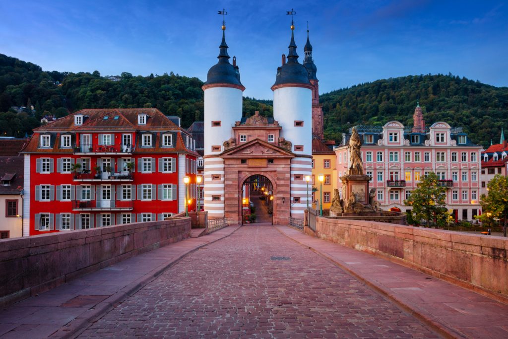 Blick über das Pflaster zur Doppelturmpforte mit Laternen und bunten Fassaden.