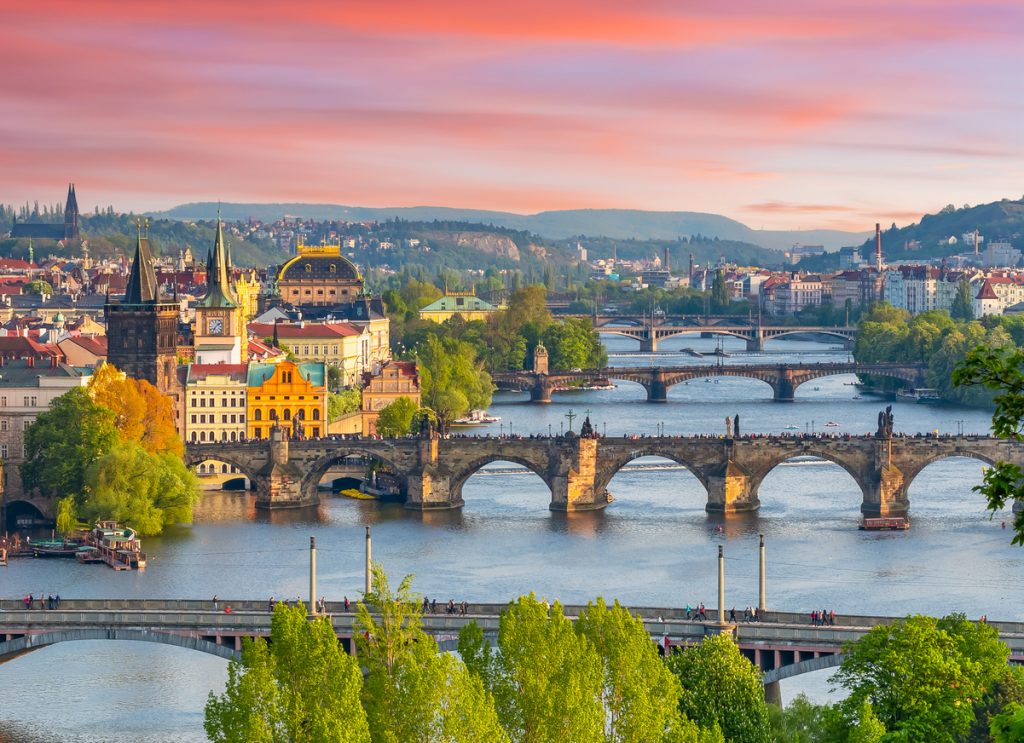 Panorama mit Karlsbrücke und weiteren Brücken vor farbigem Himmel über der Altstadt.