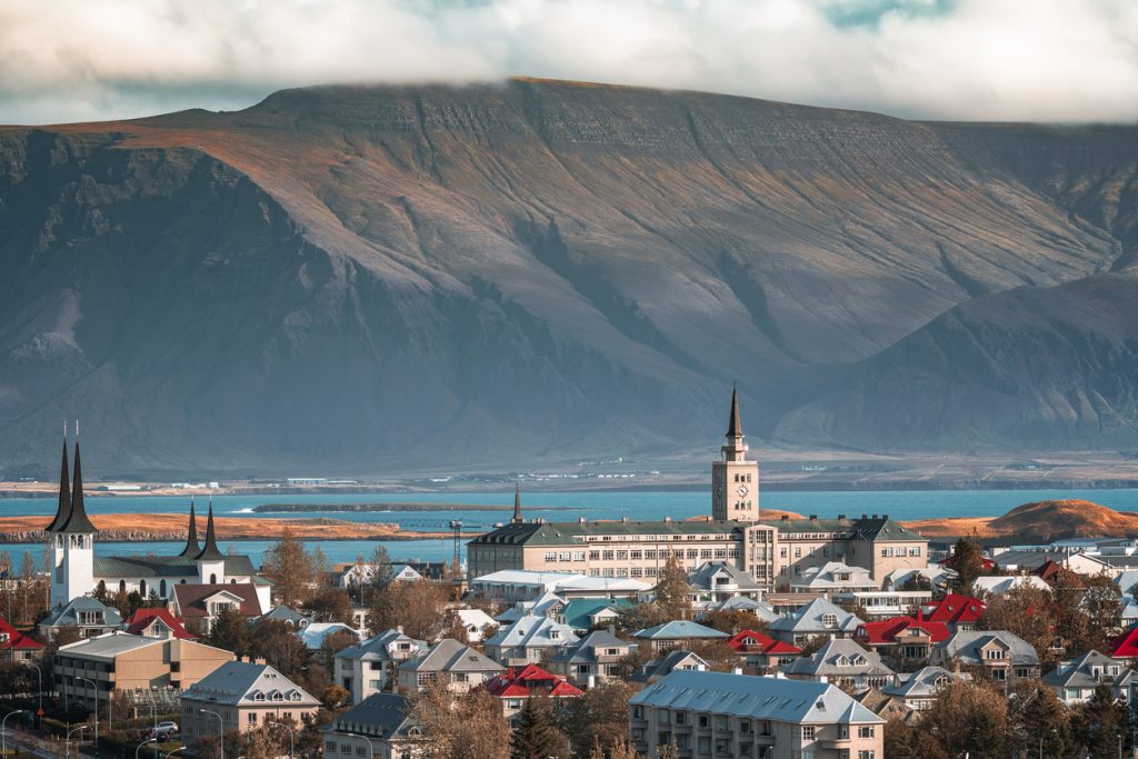 Stadtpanorama mit Kirchtürmen, Meer und dem Berg Esja im Hintergrund.