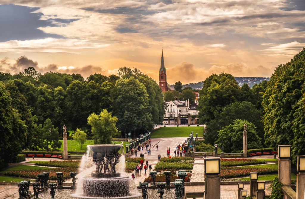 Vigeland-Brunnen im Frognerpark in Oslo bei Abendlicht mit Allee und Kirchturm.