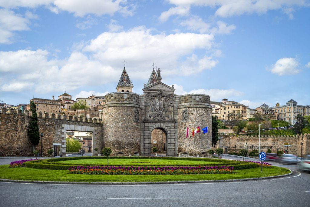 Steinernes Tor Puerta de Bisagra mit zwei Rundtürmen, Flaggen und Blumenrondell in Toledo.