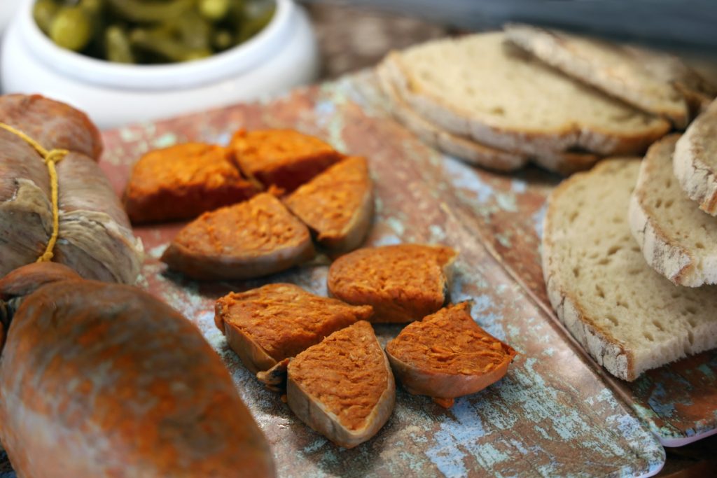 Geschnittene mallorquinische Sobrassada liegt auf einem Brett neben Brotscheiben.