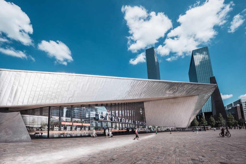 Modernes spitzes Dach und Glasfassade des Bahnhofs Rotterdam Centraal unter blauem Himmel.