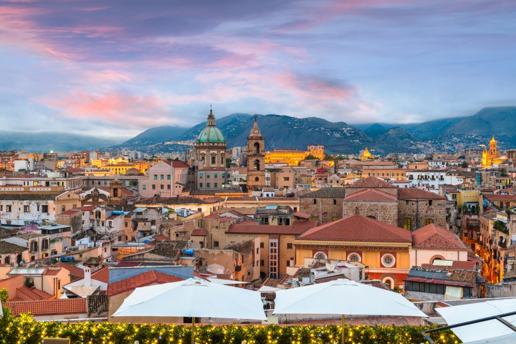 Panorama mit Dächern, Kuppeln und Bergen im Abendlicht über Palermo.