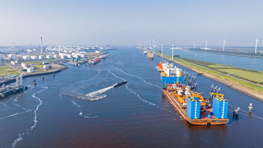 Luftbild mit Frachtschiffen, Tanks, Windrädern und breitem Fahrwasser im Hafen Rotterdam.